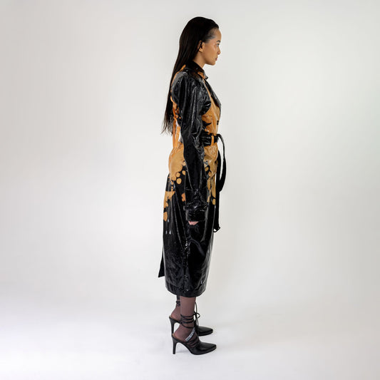 SWIM TRENCH COAT side profile on a model: knee-length black trench with peach bleached print, belt hanging at the side