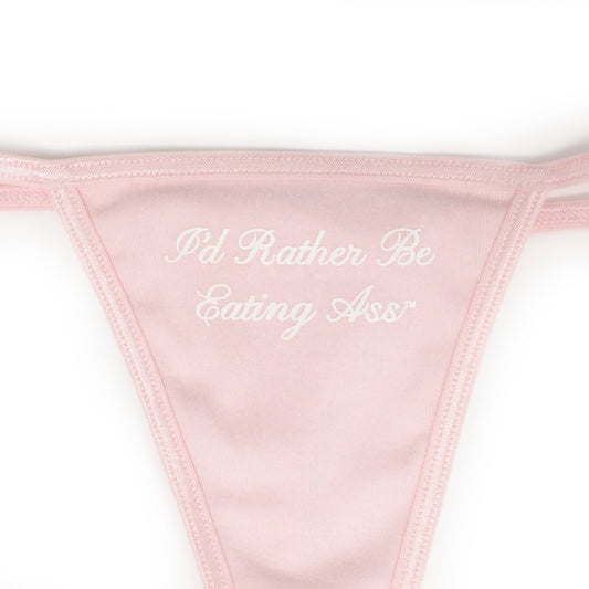 I'D RATHER BE EATING ASS CURSIVE THONG, close-up of the white screen-printed cursive "I'd Rather Be Eating Ass" on pink
