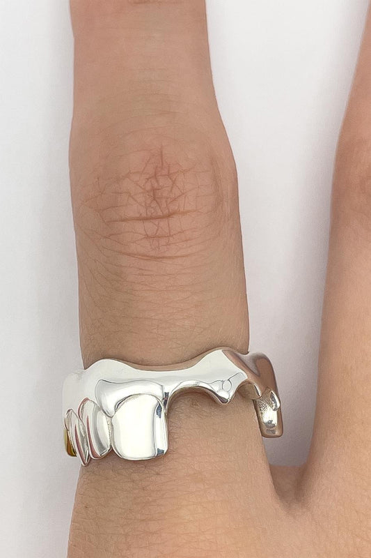 BOXER RING on a finger, top view: polished silver band shaped as a row of teeth with a gap and a gold tooth at the side