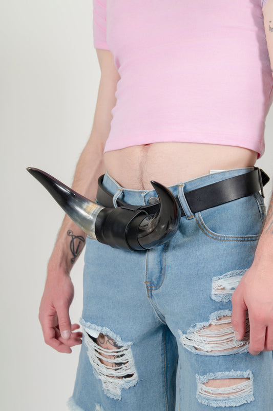 HORN BELT, close-up on a model: black leather belt with a curved cow horn buckle, worn on ripped light denim