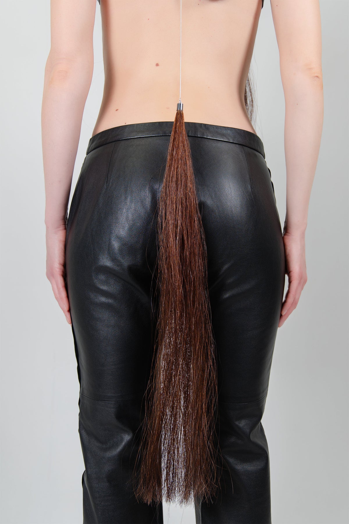 HORSE HAIR REVERSE NECKLACE (CHESTNUT), close-up: chestnut horse hair tassel falling from the chain over black trousers