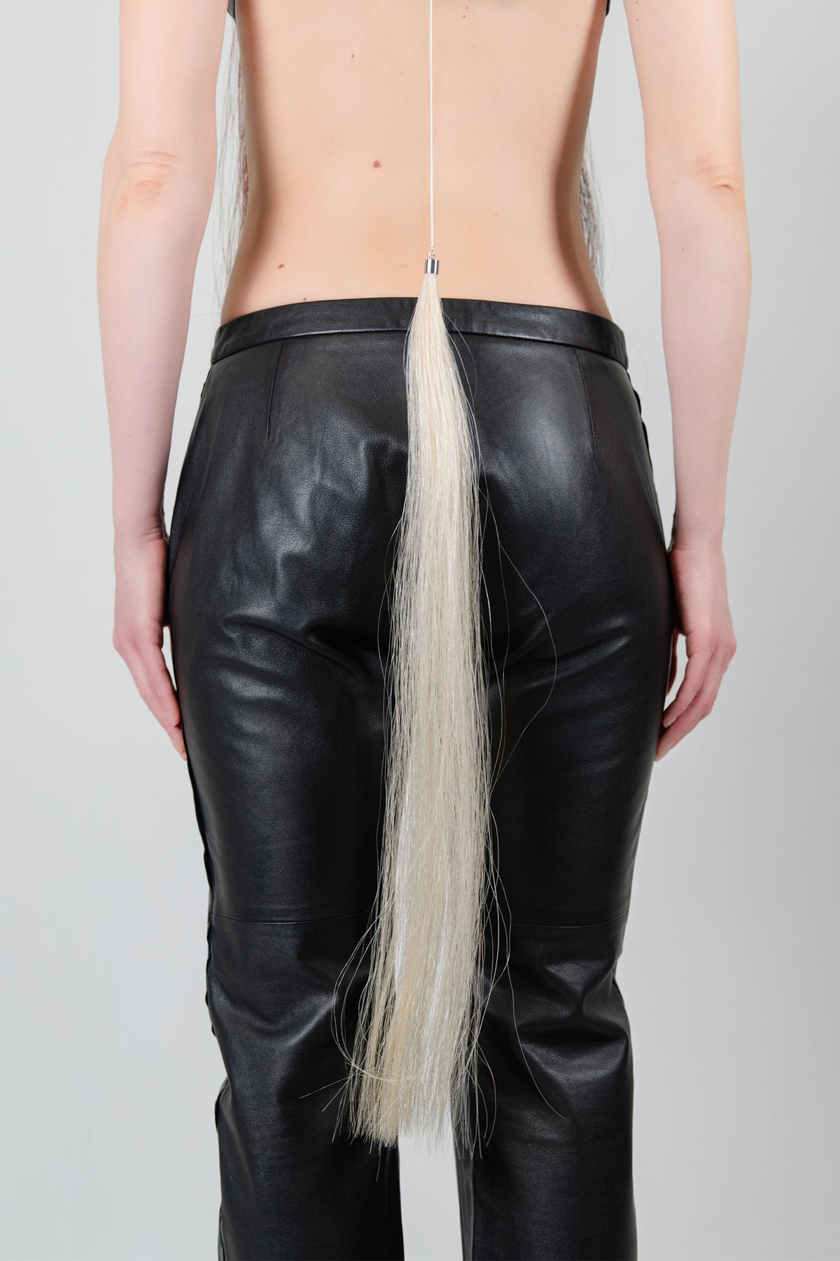 HORSE HAIR REVERSE NECKLACE (BUTTERMILK), close-up: buttermilk horse hair tassel hanging over black trousers