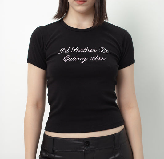 I'D RATHER BE EATING ASS CURSIVE BABY TEE on a model: skin-tight black tee, white cursive "I'd Rather Be Eating Ass" on chest