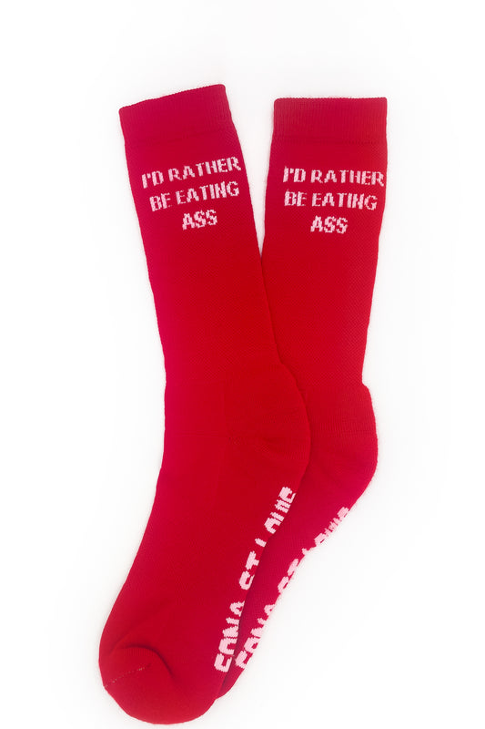 I'D RATHER BE EATING ASS SOCKS, pair laid flat: red crew socks with pink slogan at the cuffs, EDNA ST LOUIS on the soles