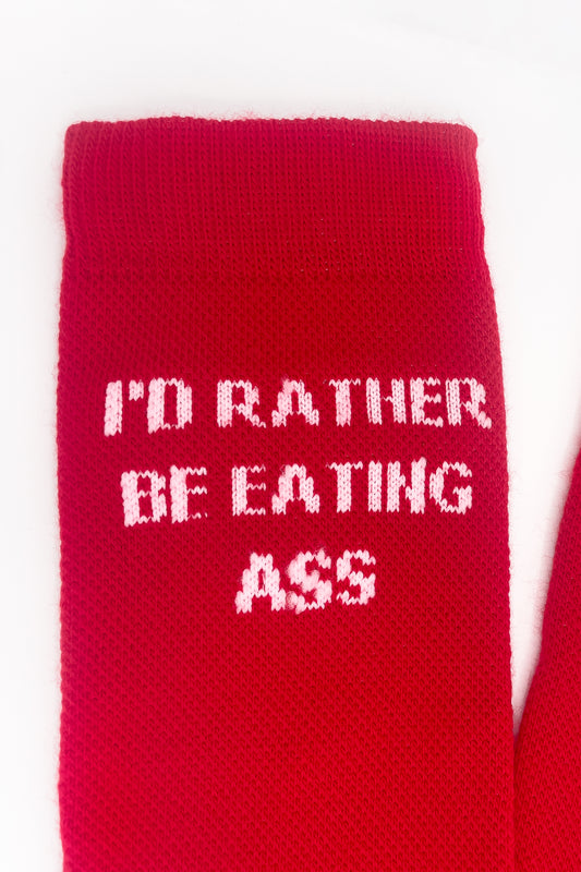 I'D RATHER BE EATING ASS SOCKS cuff close-up: pink knit "I'D RATHER BE EATING ASS" on red