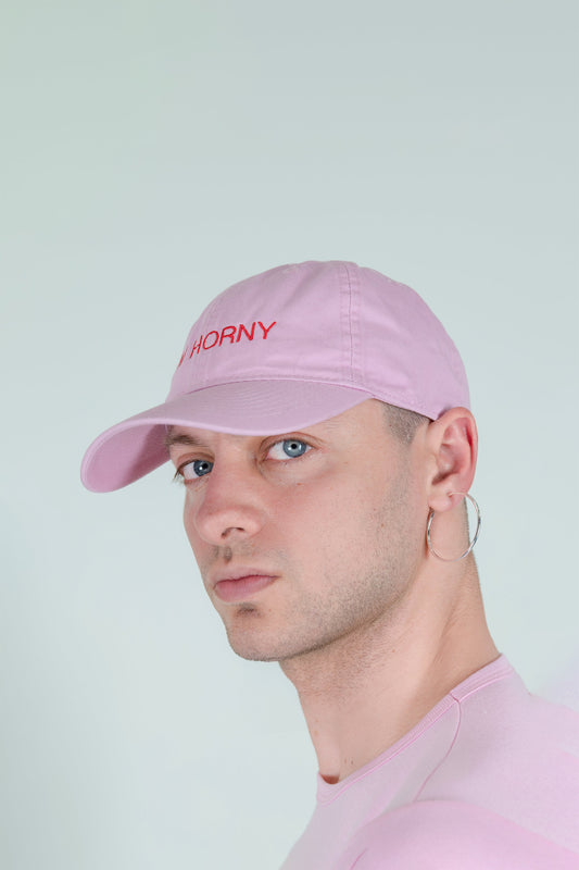 I'M HORNY BASEBALL CAP, three-quarter side view on a model, light pink with red lettering on the front panel