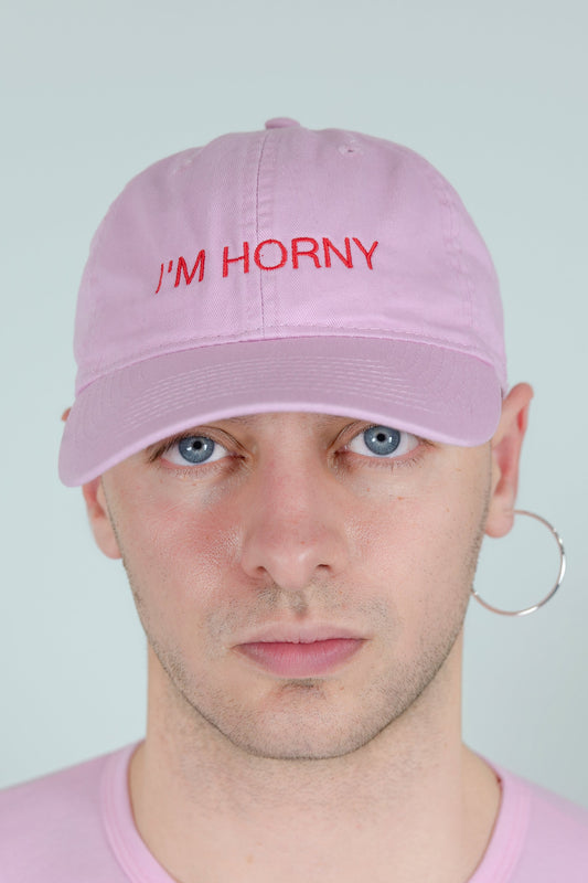 I'M HORNY BASEBALL CAP, front view on a model in a pink tee, red “I'M HORNY” graphic centred above the brim