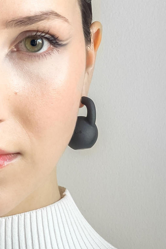 KETTLEBELL EARRINGS on a model, half-face crop: a black kettlebell hangs from the ear above a white ribbed collar