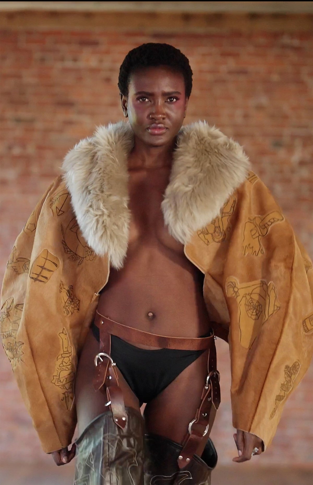 LOOK 3, Save A Horse, Ride A Cowboy: waist-up, burnt tattoos on the tan jacket, shaggy cream collar worn open