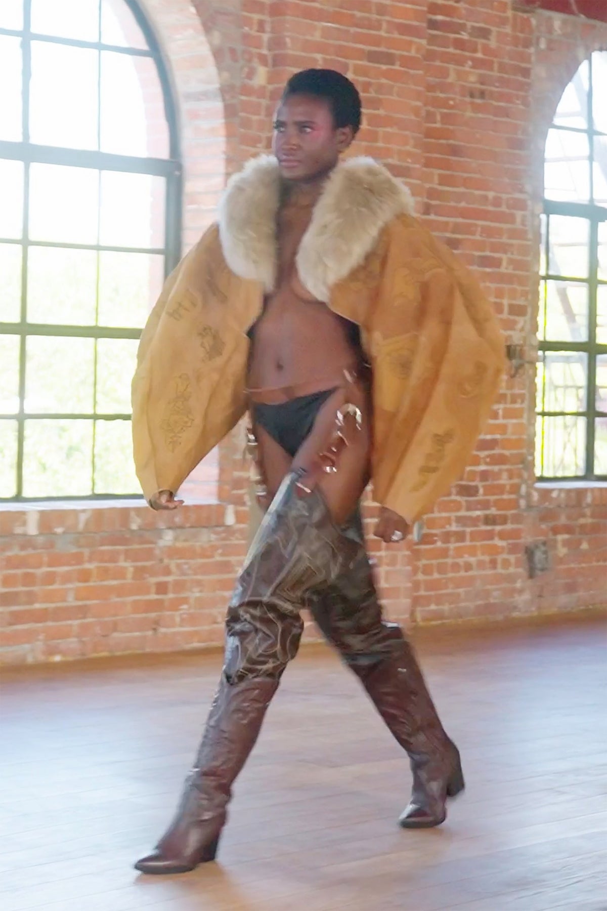 LOOK 3, Save A Horse, Ride A Cowboy: three-quarter view walking by arched windows, wide tan jacket and boot chaps