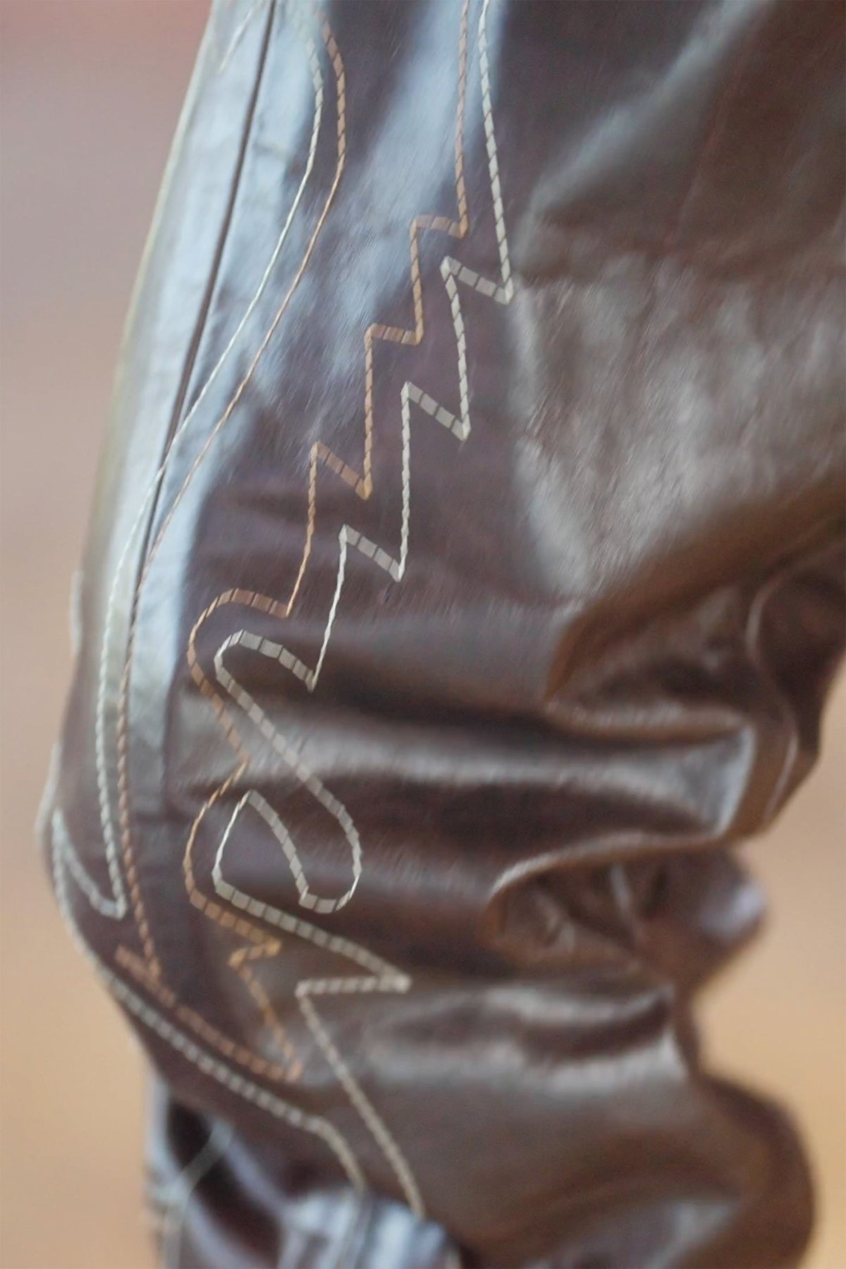 LOOK 3, Save A Horse, Ride A Cowboy: close-up of a boot chap's brown upper with pale zigzag western stitching