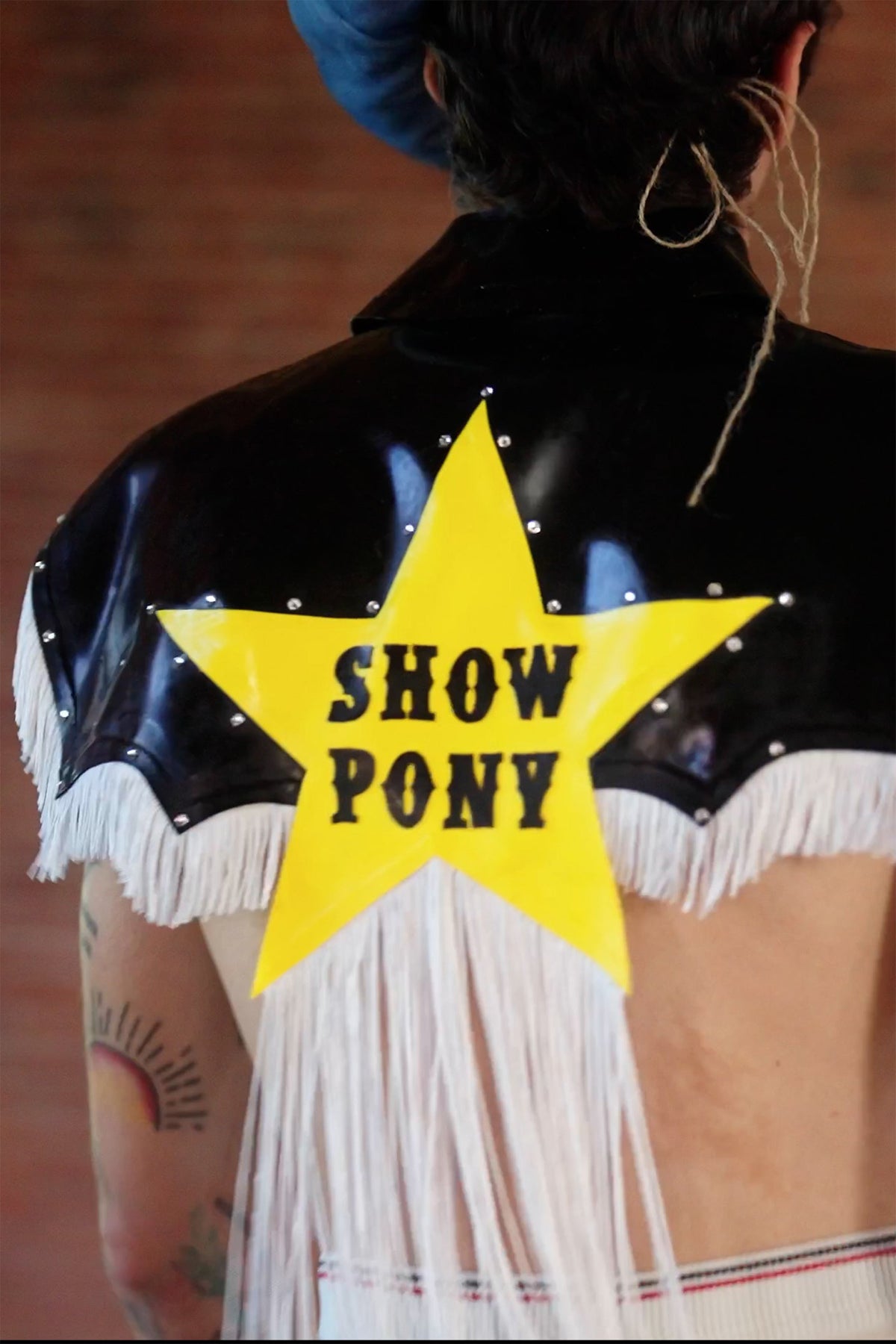 LOOK 4, Save A Horse, Ride A Cowboy: back of the latex top, yellow star reading "SHOW PONY" above long white fringe