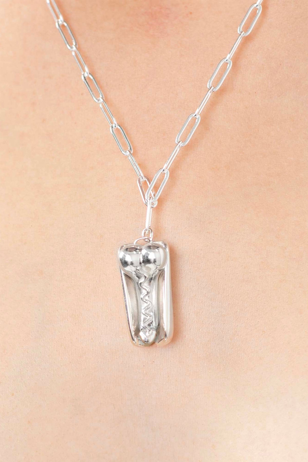 PENIS HOT DOG NECKLACE, closer view on the chest: silver pendant with zigzag mustard detail on a paperclip chain