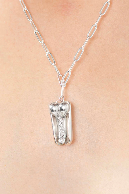 PENIS HOT DOG NECKLACE, closer view on the chest: silver pendant with zigzag mustard detail on a paperclip chain