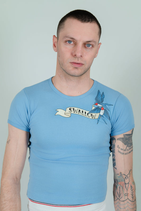 SWALLOW T-SHIRT on a model, front view: light blue baby tee with two swallows and a “SWALLOW” banner graphic on the chest