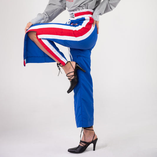 BOX TRACK PANT, model lifting one leg out through the open side slit, red and white stripe across the thigh